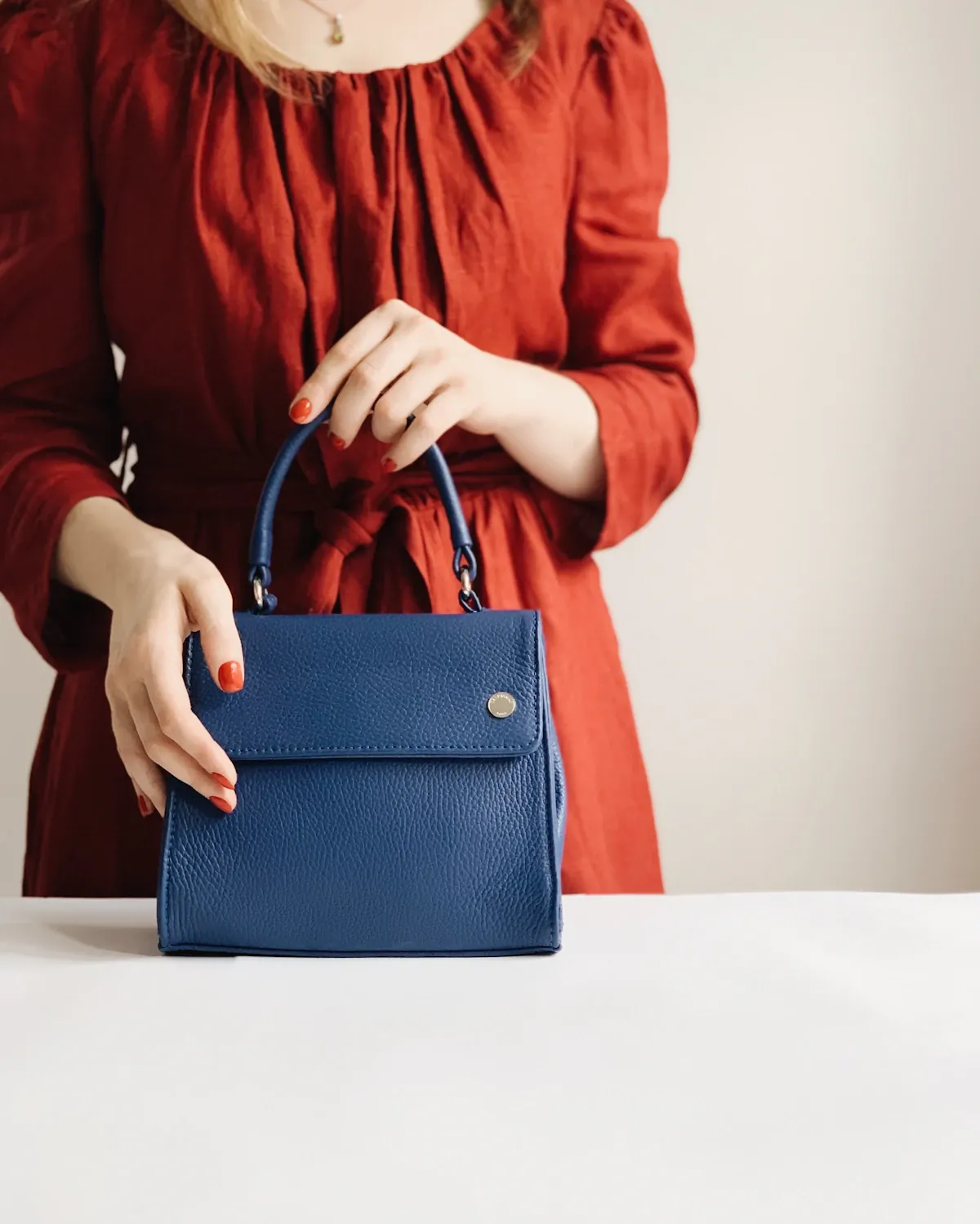 A person in a rust-coloured blouse holding a blue structured handbag.