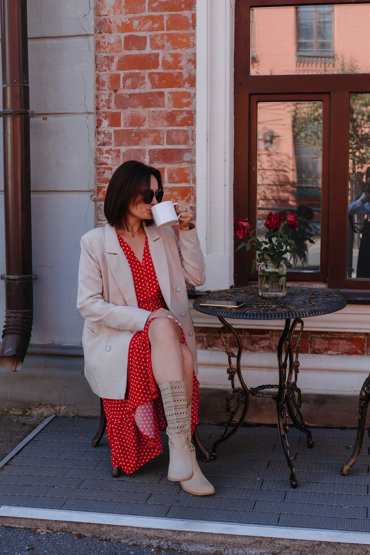 A woman in a red outfit and pale outer layer beside an outdoor cafe table.