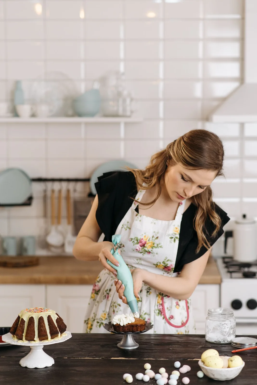 A woman decorating a cake at a kitchen work surface.