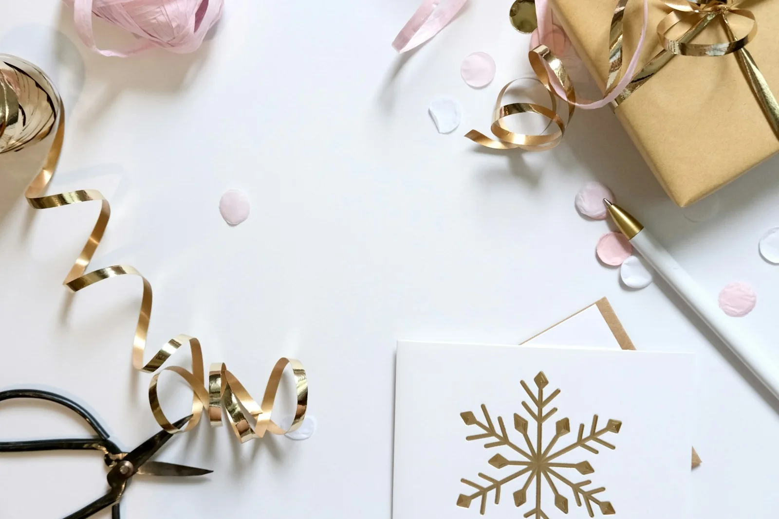 Pale wrapping paper, scissors, gold ribbon and a snowflake card on a light surface.