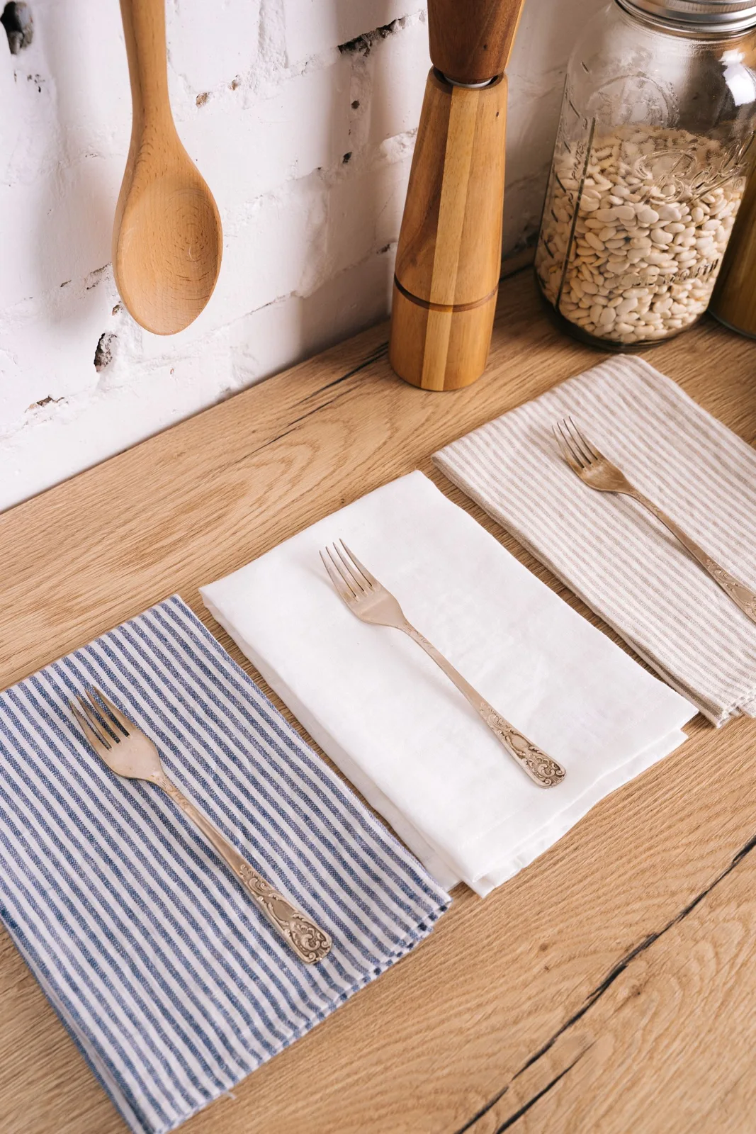 Folded cloths and silver cutlery arranged on a wooden kitchen surface.