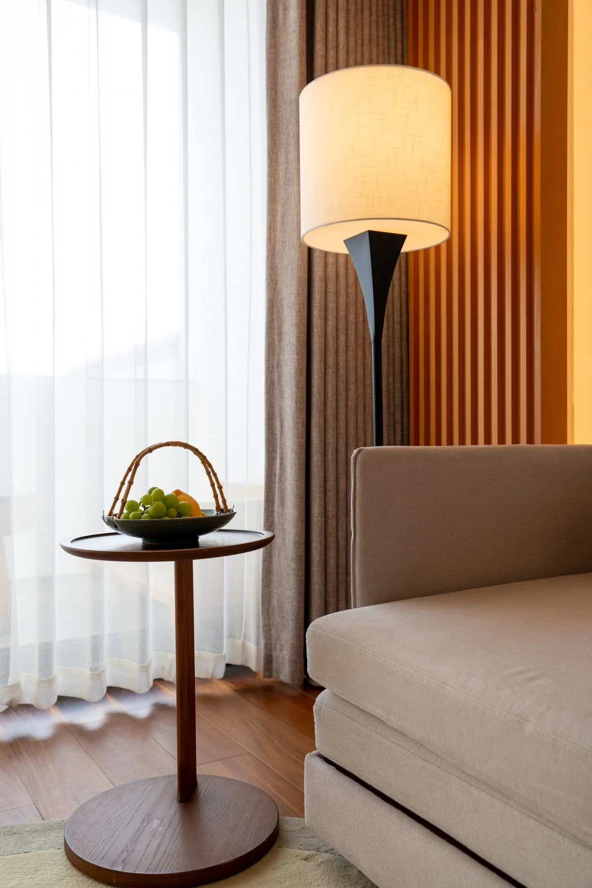 A side table and lamp beside a sofa in a bright living room.