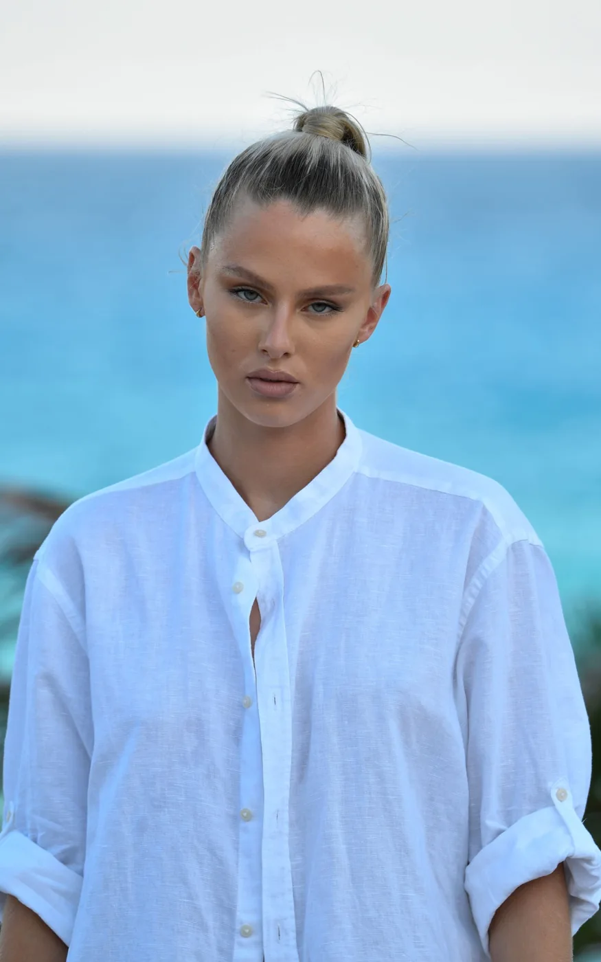 A woman wearing a white band-collar shirt beside the sea.