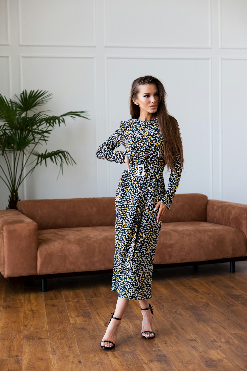 A woman in a patterned long dress beside a brown sofa.