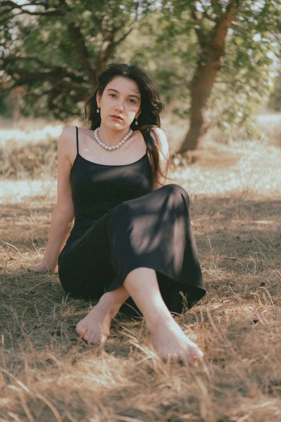 A woman seated on grass wearing a black strappy dress.