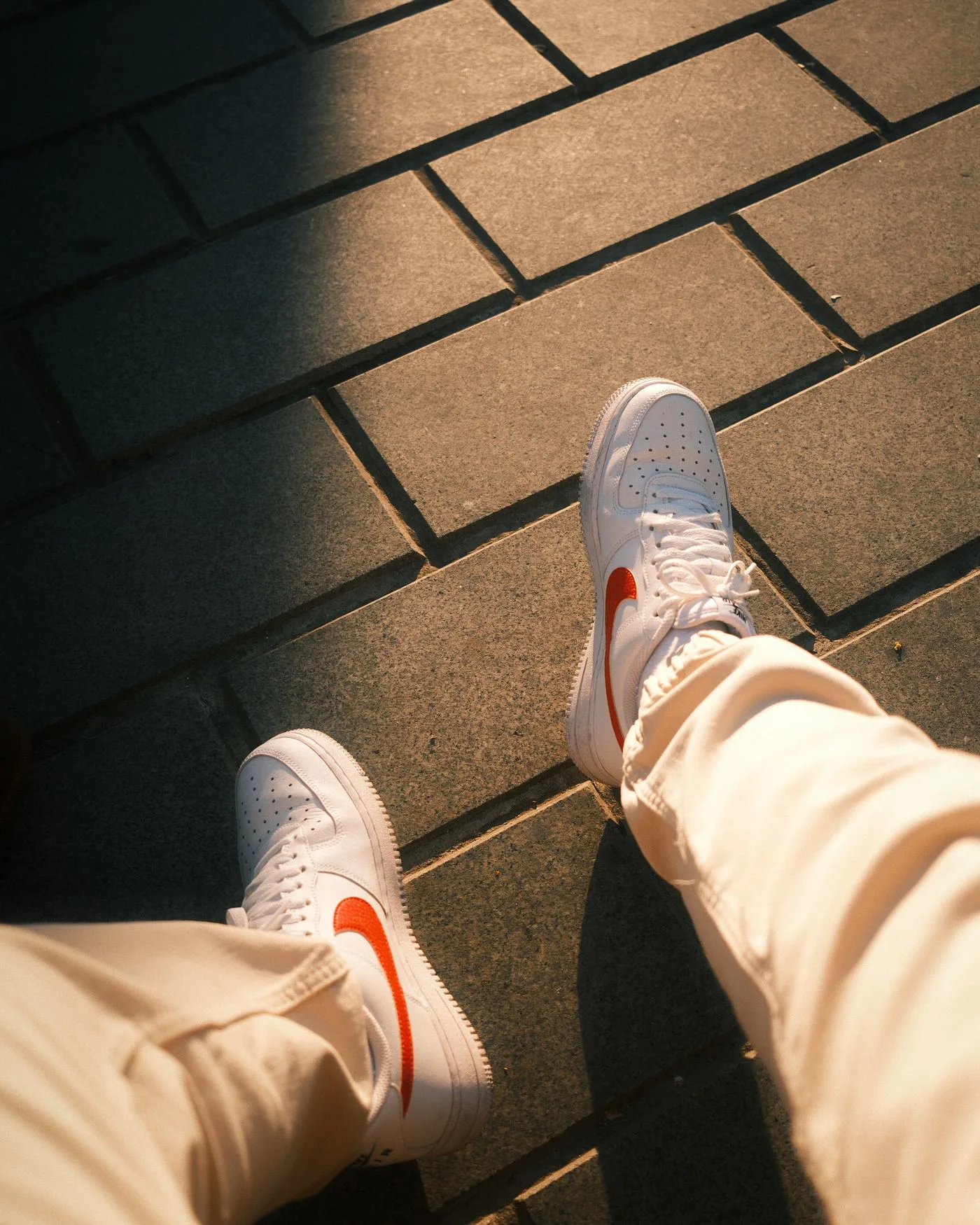 Pale sneakers with red accents beside tan trouser hems.