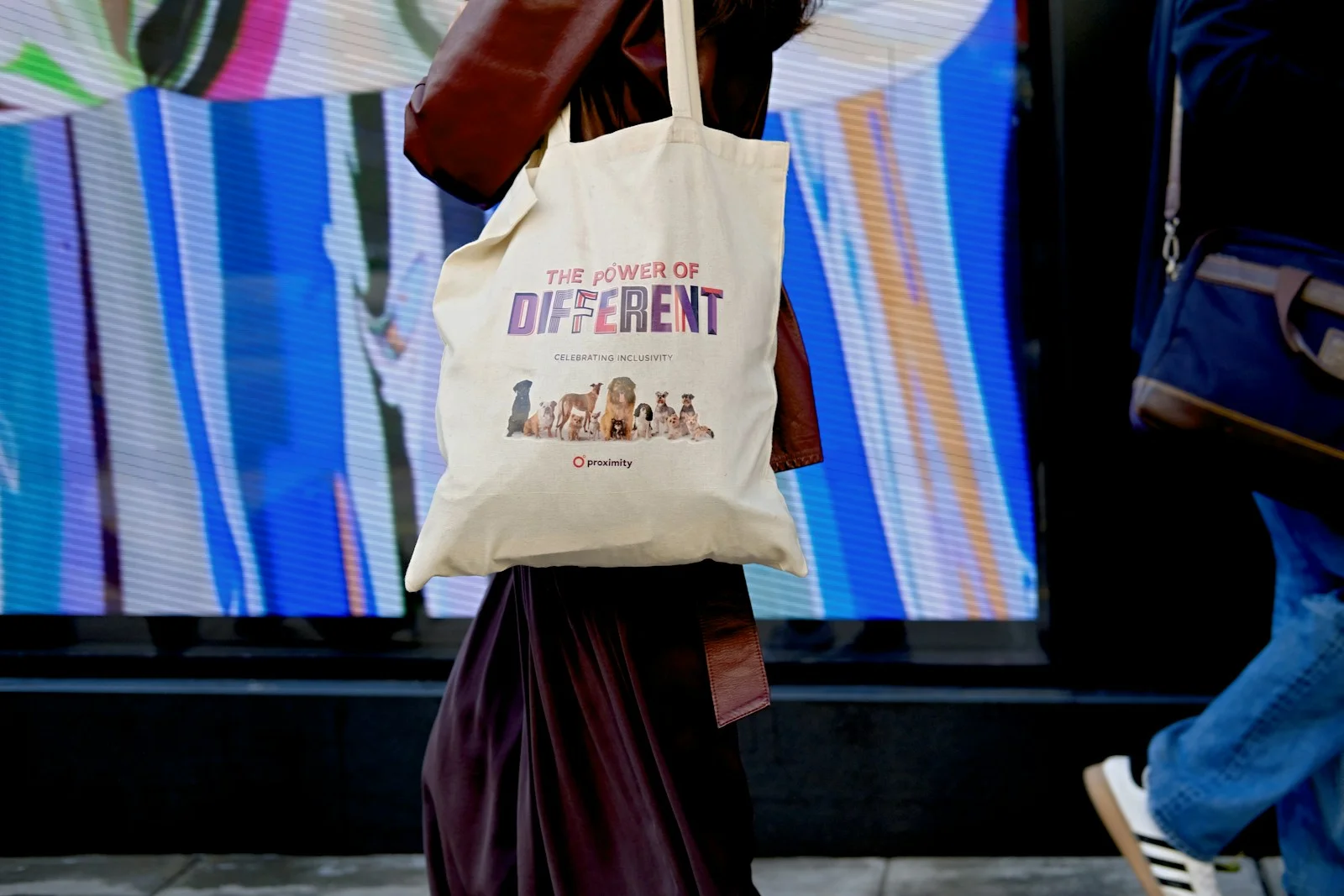 A pale printed tote carried beside a colourful wall.